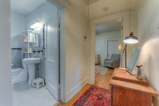 hallway featuring sink, light wood-type flooring, and tile walls