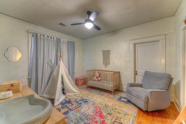 bedroom featuring a crib, hardwood / wood-style flooring, ornamental molding, and ceiling fan