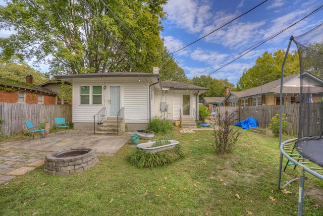 back of property with a trampoline, a patio area, a fire pit, and a lawn