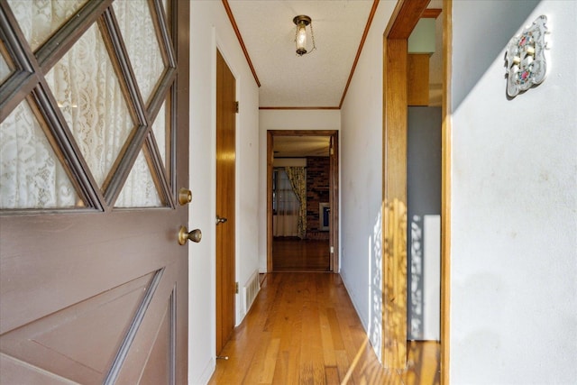 hall featuring light hardwood / wood-style floors, ornamental molding, and a textured ceiling