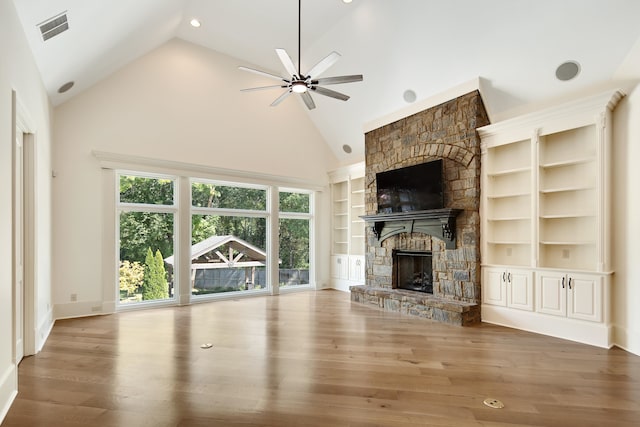 unfurnished living room with ceiling fan, built in shelves, high vaulted ceiling, a fireplace, and hardwood / wood-style floors