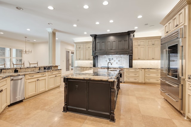 kitchen with hanging light fixtures, a center island with sink, cream cabinetry, appliances with stainless steel finishes, and light stone countertops