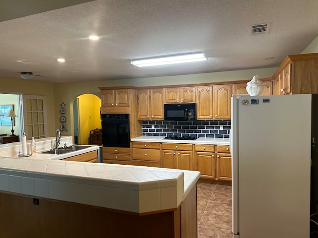 kitchen featuring sink, a kitchen island with sink, backsplash, tile counters, and black appliances