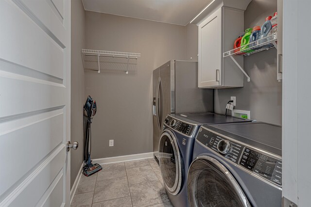 clothes washing area with washer and clothes dryer, light tile patterned floors, and cabinets