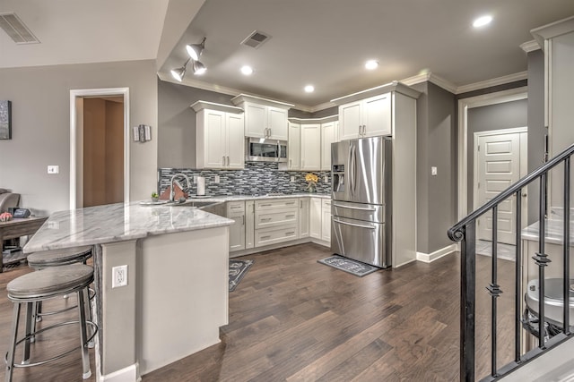 kitchen with appliances with stainless steel finishes, light stone countertops, kitchen peninsula, a breakfast bar, and white cabinetry