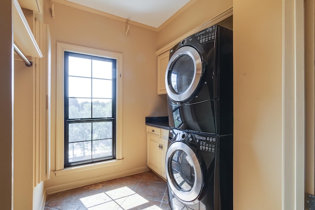 clothes washing area with cabinets, stacked washer and clothes dryer, and ornamental molding