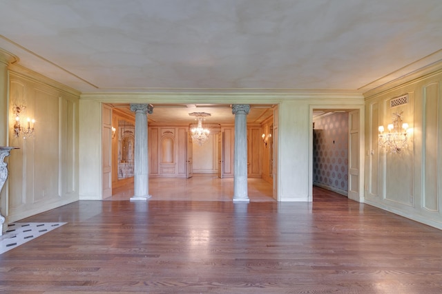 unfurnished room with ornate columns, wood-type flooring, ornamental molding, and a notable chandelier