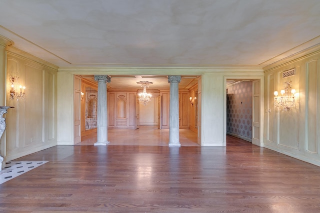 unfurnished living room featuring a chandelier, ornate columns, wood finished floors, and a decorative wall