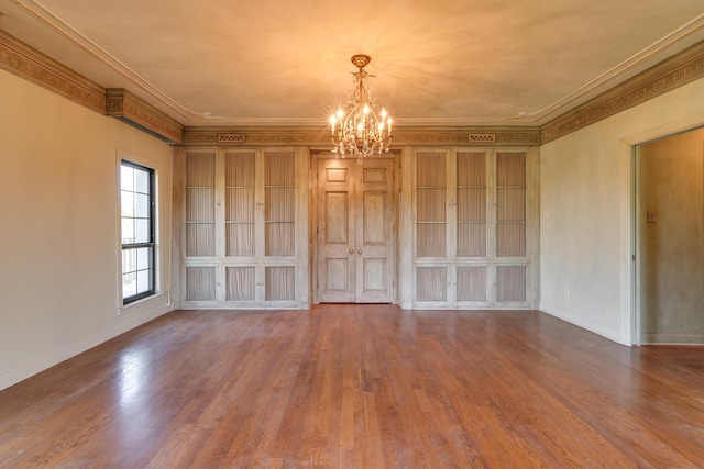 unfurnished room with ornamental molding, an inviting chandelier, wood finished floors, and baseboards