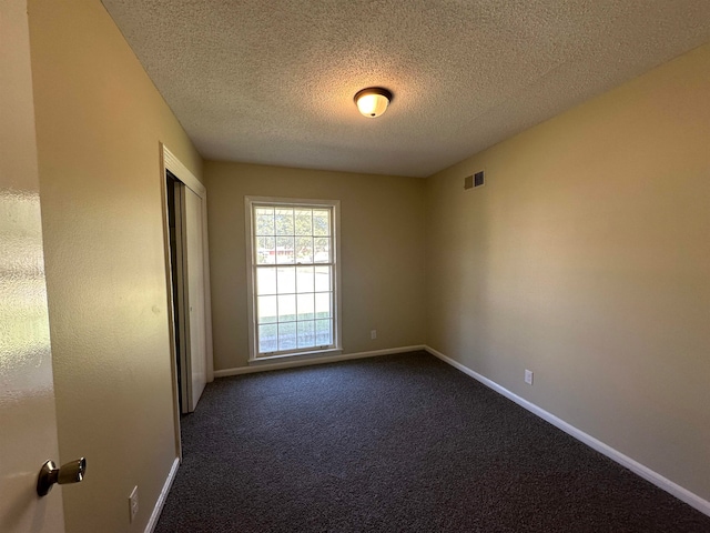 empty room with a textured ceiling and dark carpet