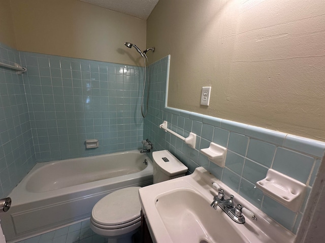 full bathroom with a textured ceiling, tile walls, toilet, vanity, and tiled shower / bath combo