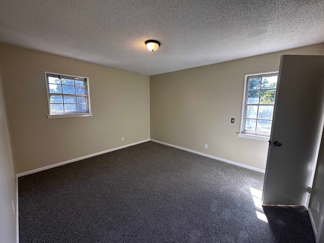 empty room featuring dark carpet, a textured ceiling, and plenty of natural light