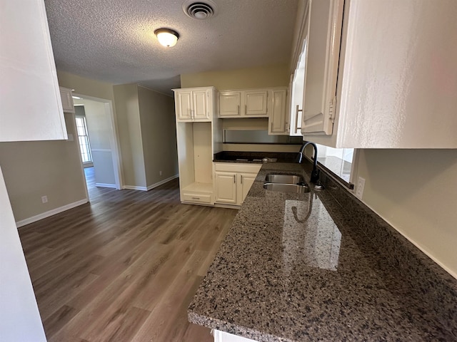 kitchen with sink, a textured ceiling, hardwood / wood-style floors, dark stone counters, and white cabinets