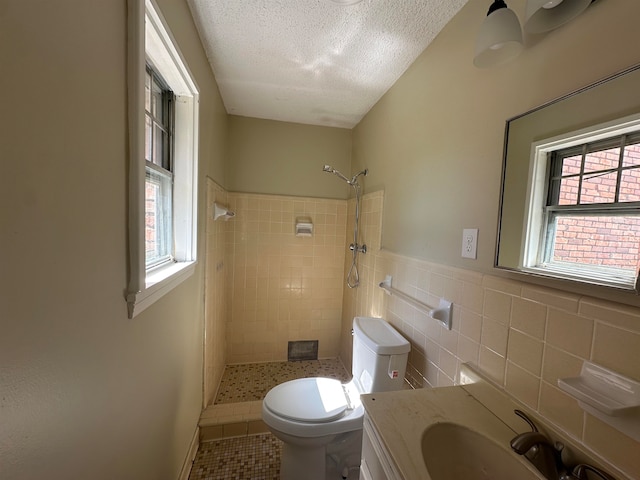 bathroom featuring toilet, tile patterned flooring, vanity, a tile shower, and a textured ceiling