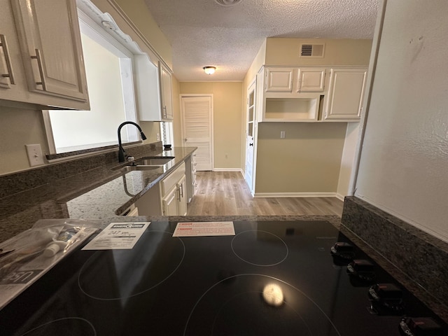 kitchen with light hardwood / wood-style floors, a textured ceiling, dark stone countertops, and sink