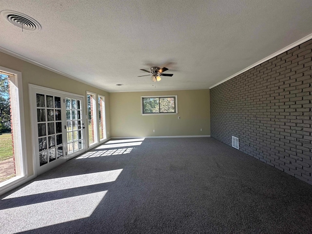 carpeted empty room featuring a textured ceiling, ceiling fan, brick wall, and a wealth of natural light