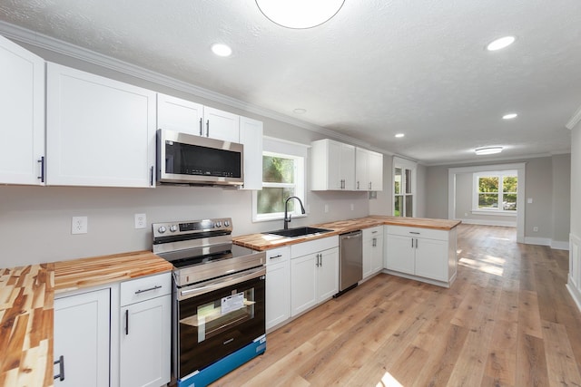 kitchen with appliances with stainless steel finishes, sink, light wood-type flooring, butcher block counters, and white cabinets