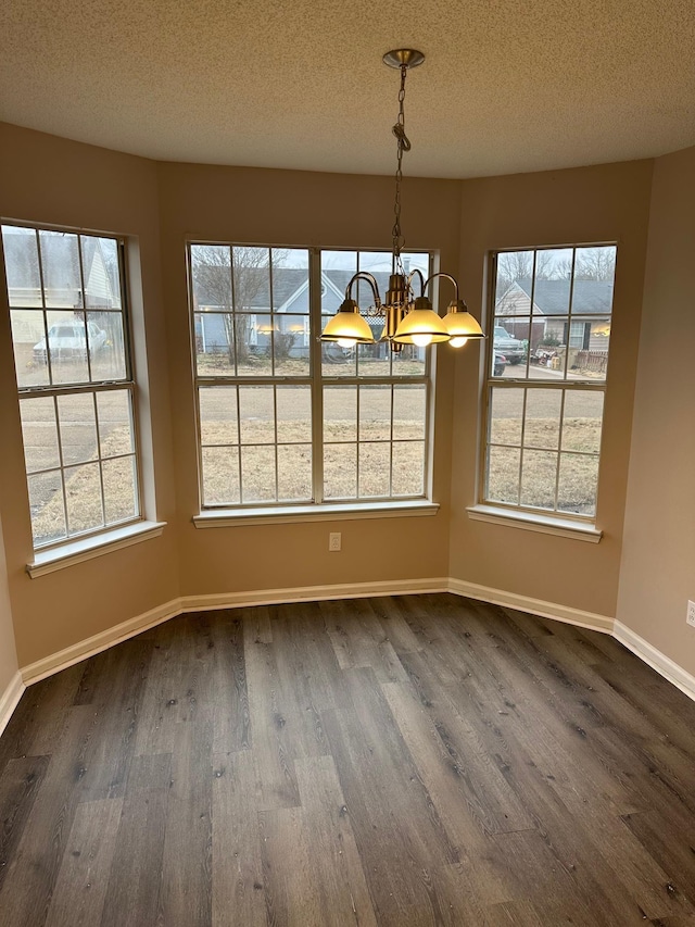 unfurnished dining area featuring a chandelier, dark wood-type flooring, a healthy amount of sunlight, and a textured ceiling