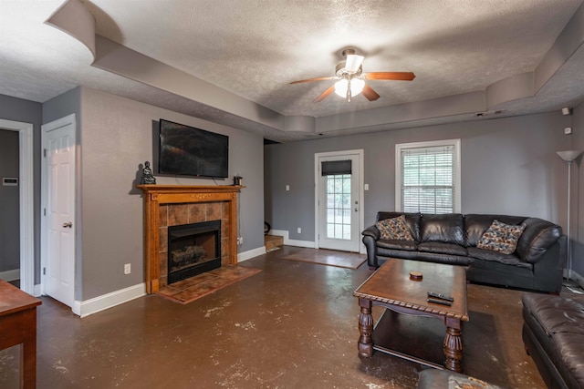 living room featuring ceiling fan, a tile fireplace, and a textured ceiling