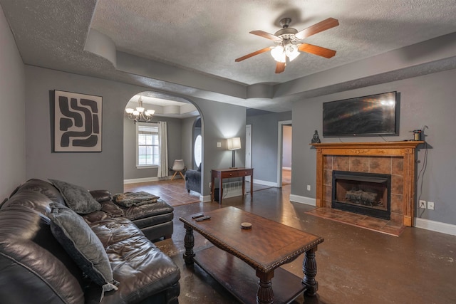 living room featuring concrete floors, a tiled fireplace, ceiling fan, a tray ceiling, and a textured ceiling