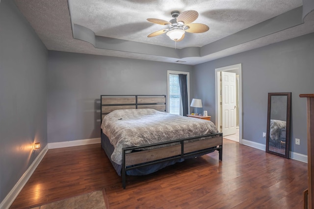 bedroom with dark hardwood / wood-style flooring, a tray ceiling, a textured ceiling, and ceiling fan