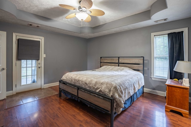 bedroom with a raised ceiling, dark wood-type flooring, ceiling fan, and multiple windows