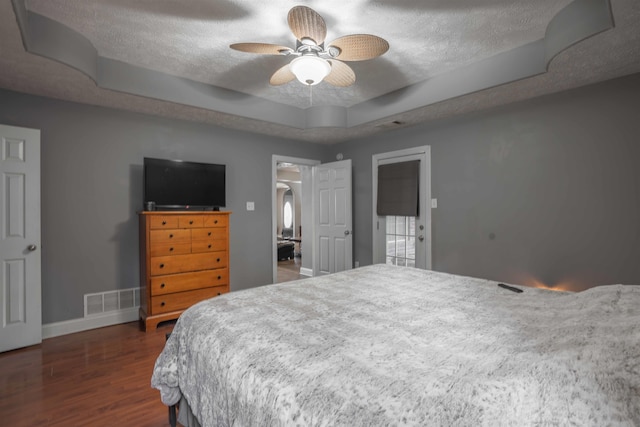 bedroom with a textured ceiling, dark wood-type flooring, a raised ceiling, and ceiling fan