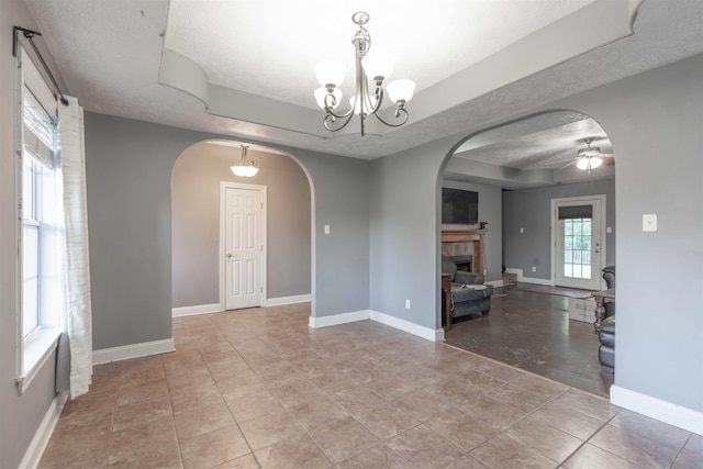 tiled empty room with a tiled fireplace, ceiling fan with notable chandelier, and a textured ceiling