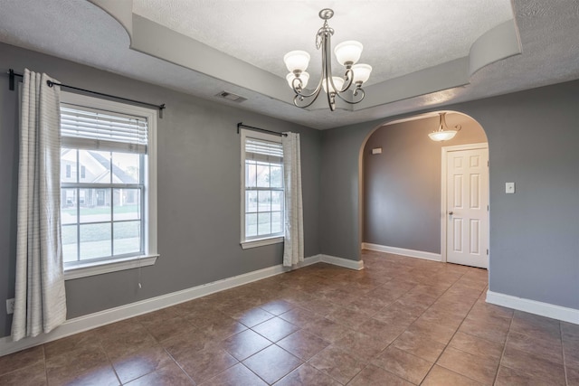 spare room with tile patterned flooring, a healthy amount of sunlight, a textured ceiling, and an inviting chandelier