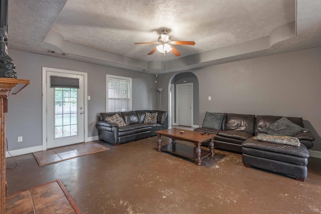 living room with a tray ceiling, a textured ceiling, and ceiling fan