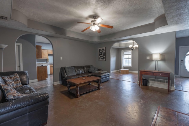 living room with a raised ceiling, ceiling fan with notable chandelier, and a textured ceiling