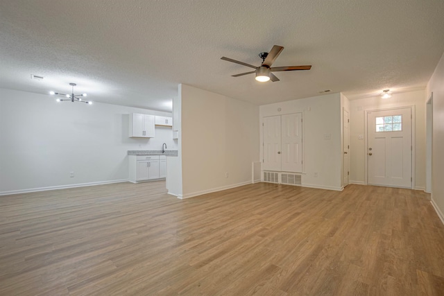 unfurnished living room featuring a textured ceiling, light wood-type flooring, and ceiling fan with notable chandelier