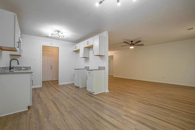 kitchen featuring sink, light wood-type flooring, white cabinetry, a textured ceiling, and ceiling fan