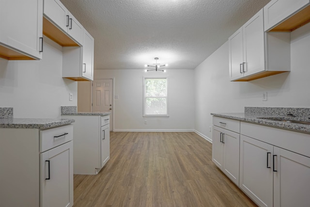 kitchen featuring white cabinetry, a textured ceiling, a chandelier, light hardwood / wood-style flooring, and light stone counters