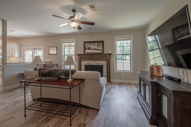 living room featuring a brick fireplace, light wood-type flooring, a healthy amount of sunlight, and ceiling fan