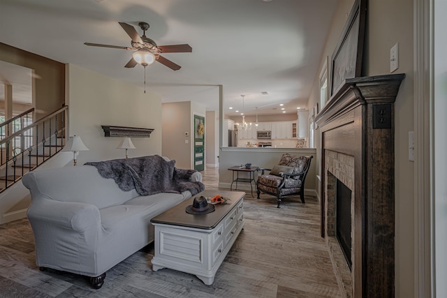 living room with light hardwood / wood-style flooring, a fireplace, and ceiling fan with notable chandelier