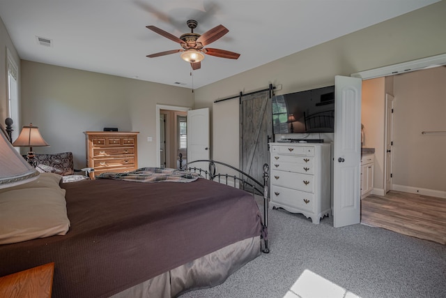 bedroom with ensuite bath, a barn door, light wood-type flooring, and ceiling fan