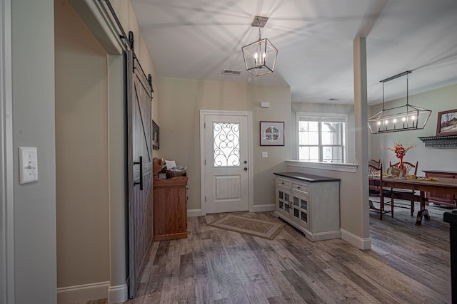 entrance foyer with a barn door, wood-type flooring, and an inviting chandelier