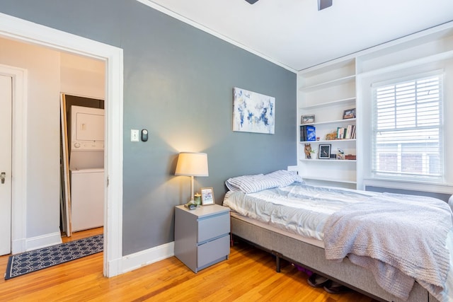 bedroom featuring ornamental molding, stacked washer and dryer, hardwood / wood-style flooring, and ceiling fan