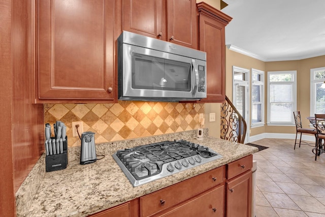 kitchen with decorative backsplash, light stone counters, light tile patterned floors, ornamental molding, and stainless steel appliances