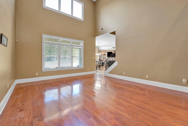 unfurnished living room with a towering ceiling, light hardwood / wood-style flooring, an inviting chandelier, and a wealth of natural light