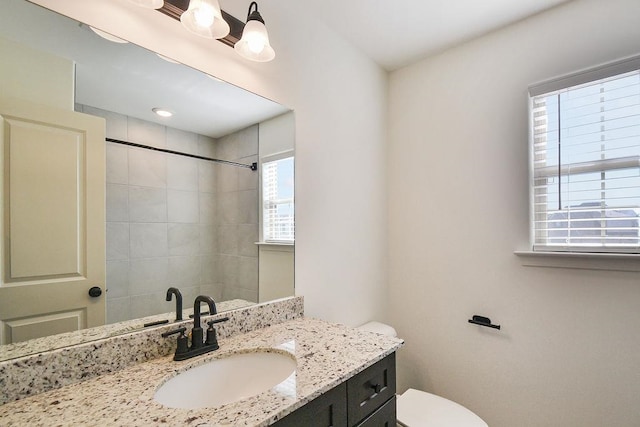 bathroom with vanity, toilet, a tile shower, and plenty of natural light