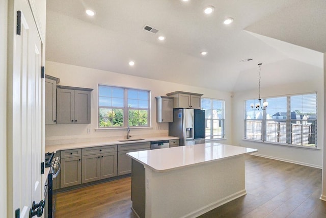 kitchen with hanging light fixtures, stainless steel appliances, sink, a center island, and vaulted ceiling