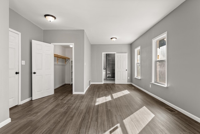 unfurnished bedroom with a spacious closet, a closet, and dark hardwood / wood-style flooring