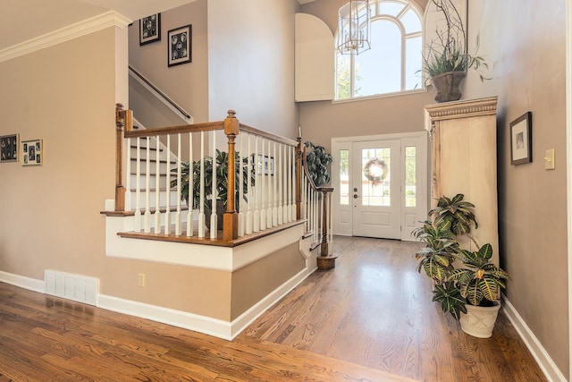 entrance foyer featuring crown molding, wood-type flooring, and a towering ceiling