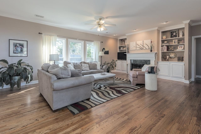 living room with hardwood / wood-style floors, ceiling fan, a high end fireplace, built in shelves, and crown molding