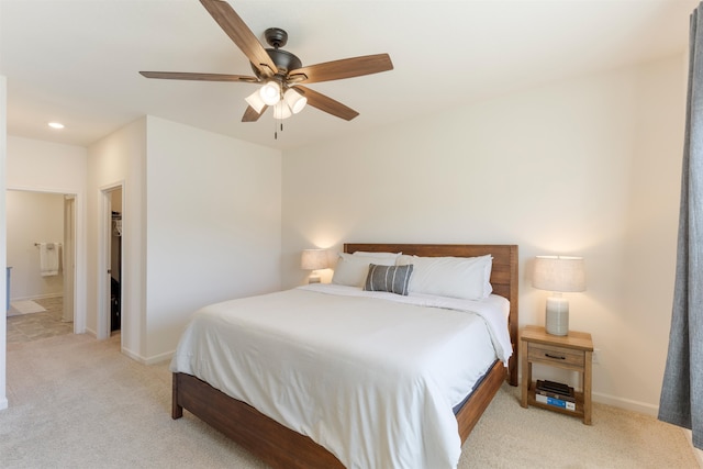 bedroom with ensuite bathroom, light colored carpet, and ceiling fan