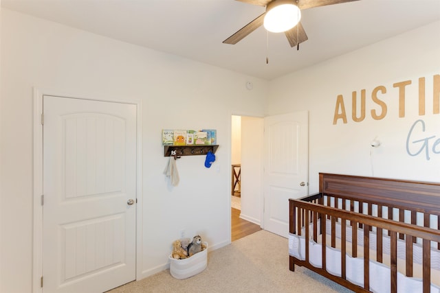 bedroom with light colored carpet, a crib, and ceiling fan