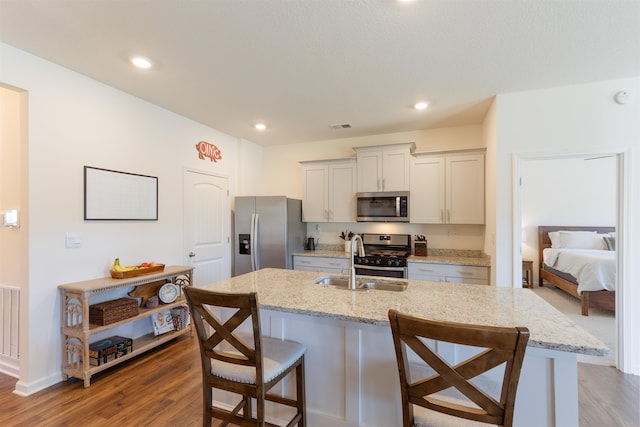 kitchen with dark hardwood / wood-style floors, stainless steel appliances, a center island with sink, sink, and light stone counters