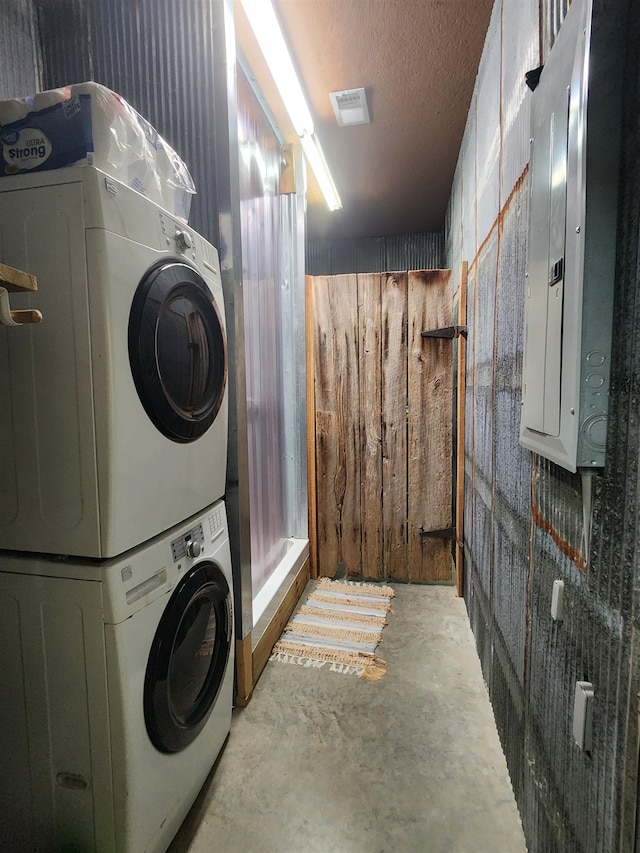 washroom with stacked washing maching and dryer, a textured ceiling, electric panel, and wooden walls